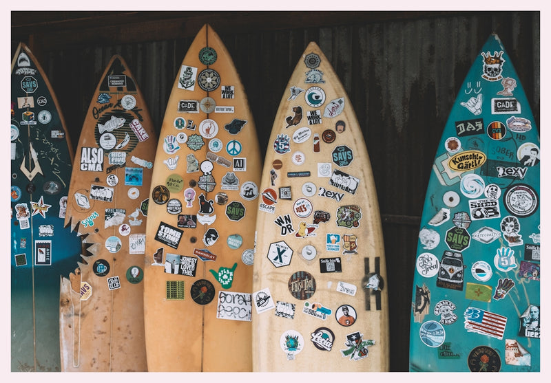 Surfboards covered in stickers lean against a wall.