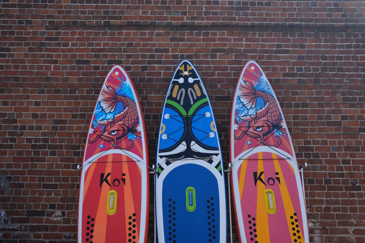 Three colorful paddleboards with designs leaning against a brick wall.